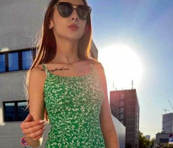 Das zierliche rumänische Escort Model Irina steht mit einem grünen Sommerkleid und Sonnenbrille bekleidet vor einem Berliner Haus