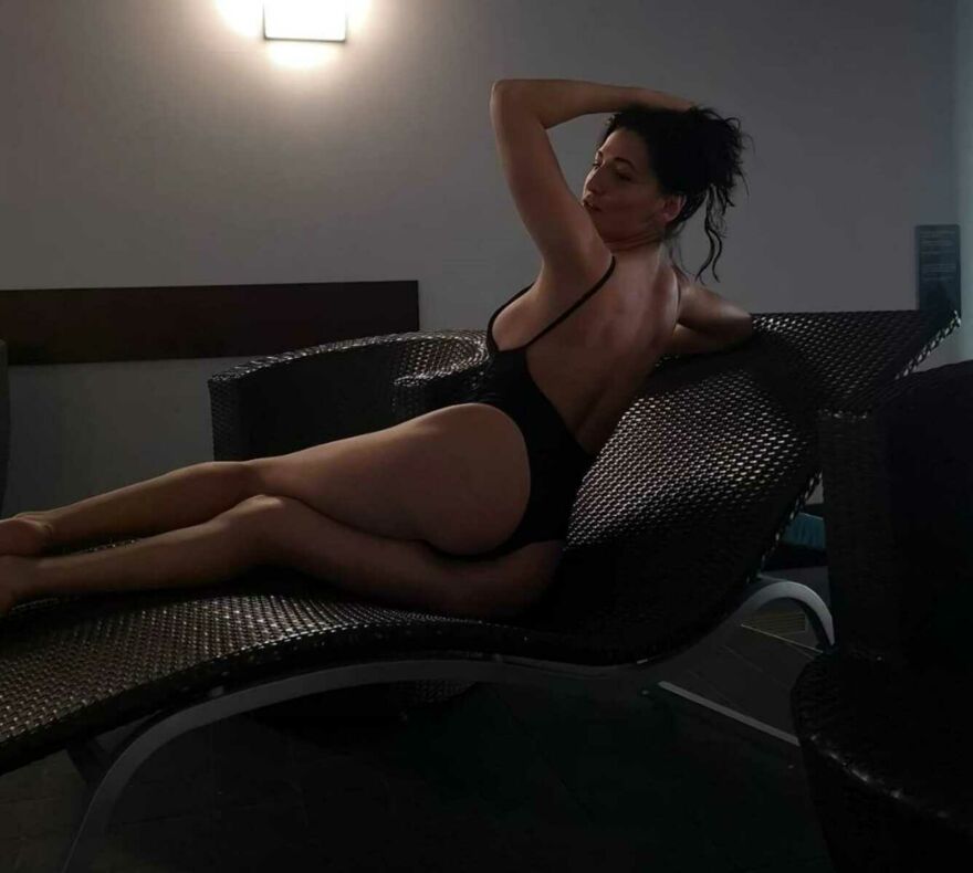 Das slovakische Escort Model Anastasia rekelt sich in engem schwarzen Badeanzug auf einem Kanapee und zeigt ihre Rückseite