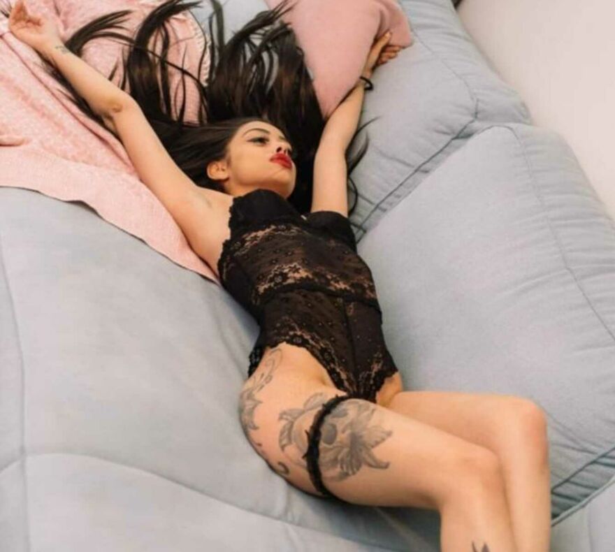 Das zierliche Escort-Girl Miren-Madlon liegt rücklings in schwarzen Negligee auf dem Bett