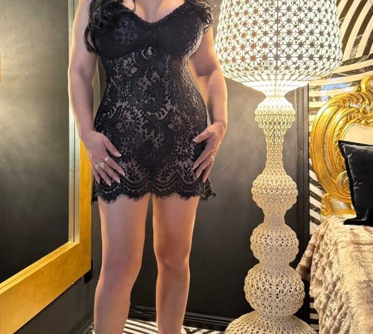 Die Hure Monika aus dem Bordell Herrenhaus Berlin steht mit schwarzen Kleid bekleidet vor der Kamera.