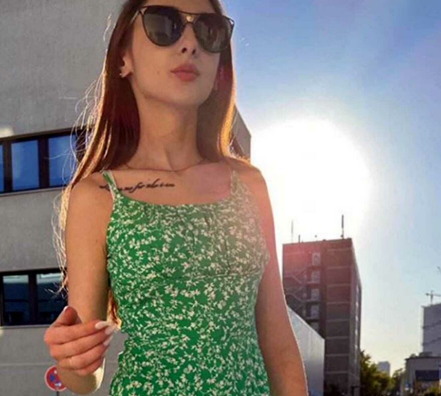 Das zierliche rumänische Escort Model Irina steht mit einem grünen Sommerkleid und Sonnenbrille bekleidet vor einem Berliner Haus